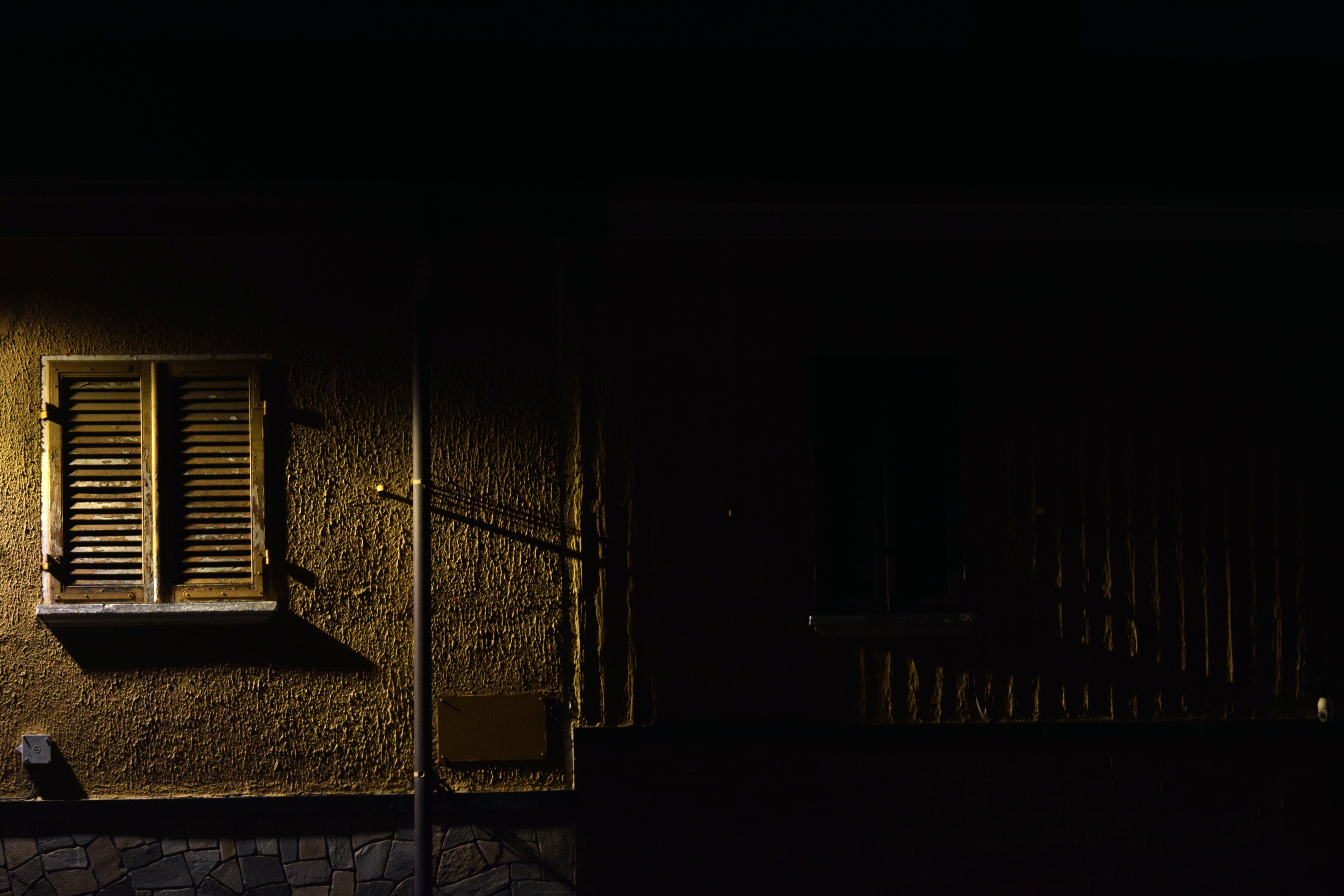  Fotografia in penombra di un edificio,persiane illuminate che proiettano ombre sul muro.