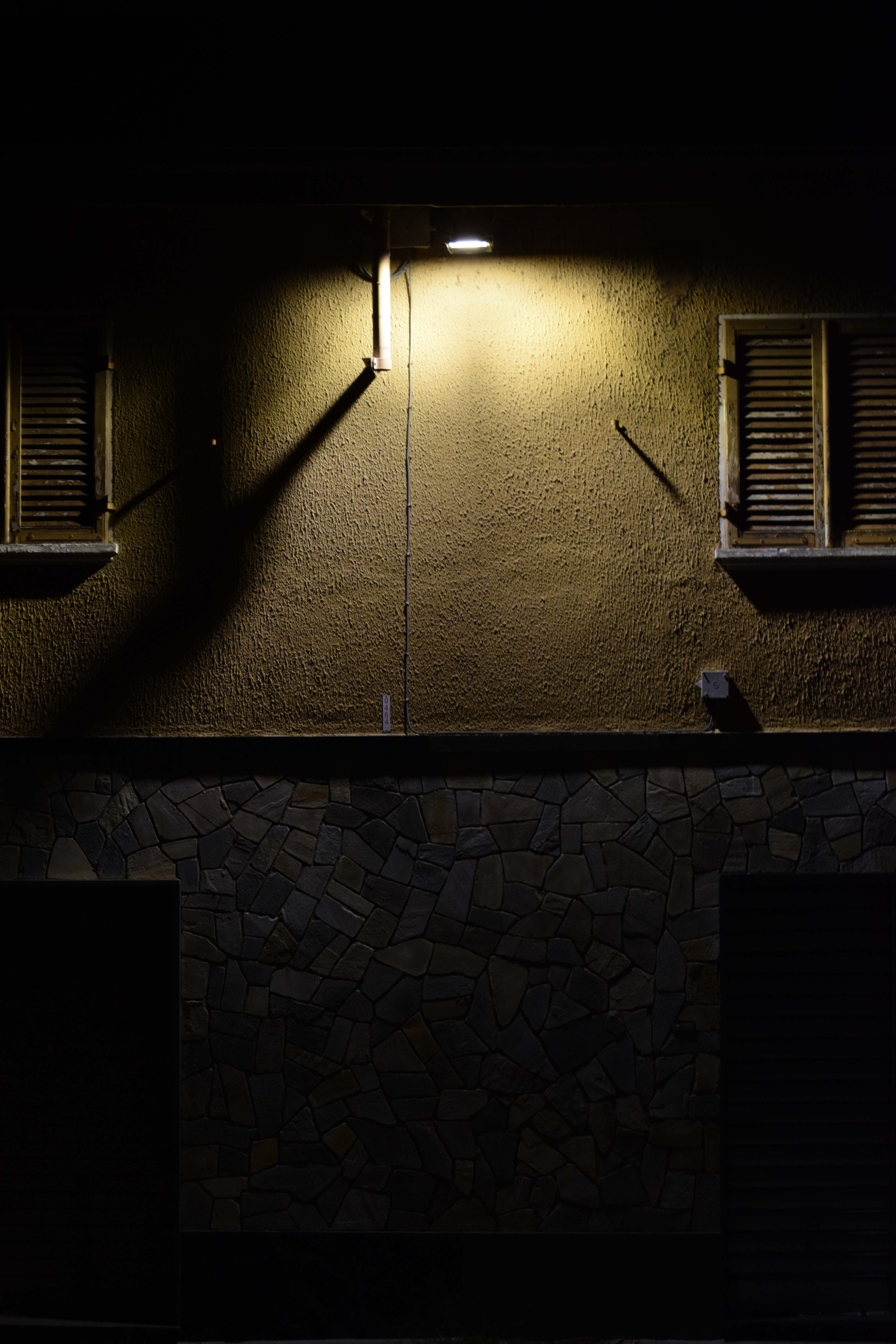 fotografia in penombra di un edificio, una luce in alto illumina i muri creando giochi di ombre.