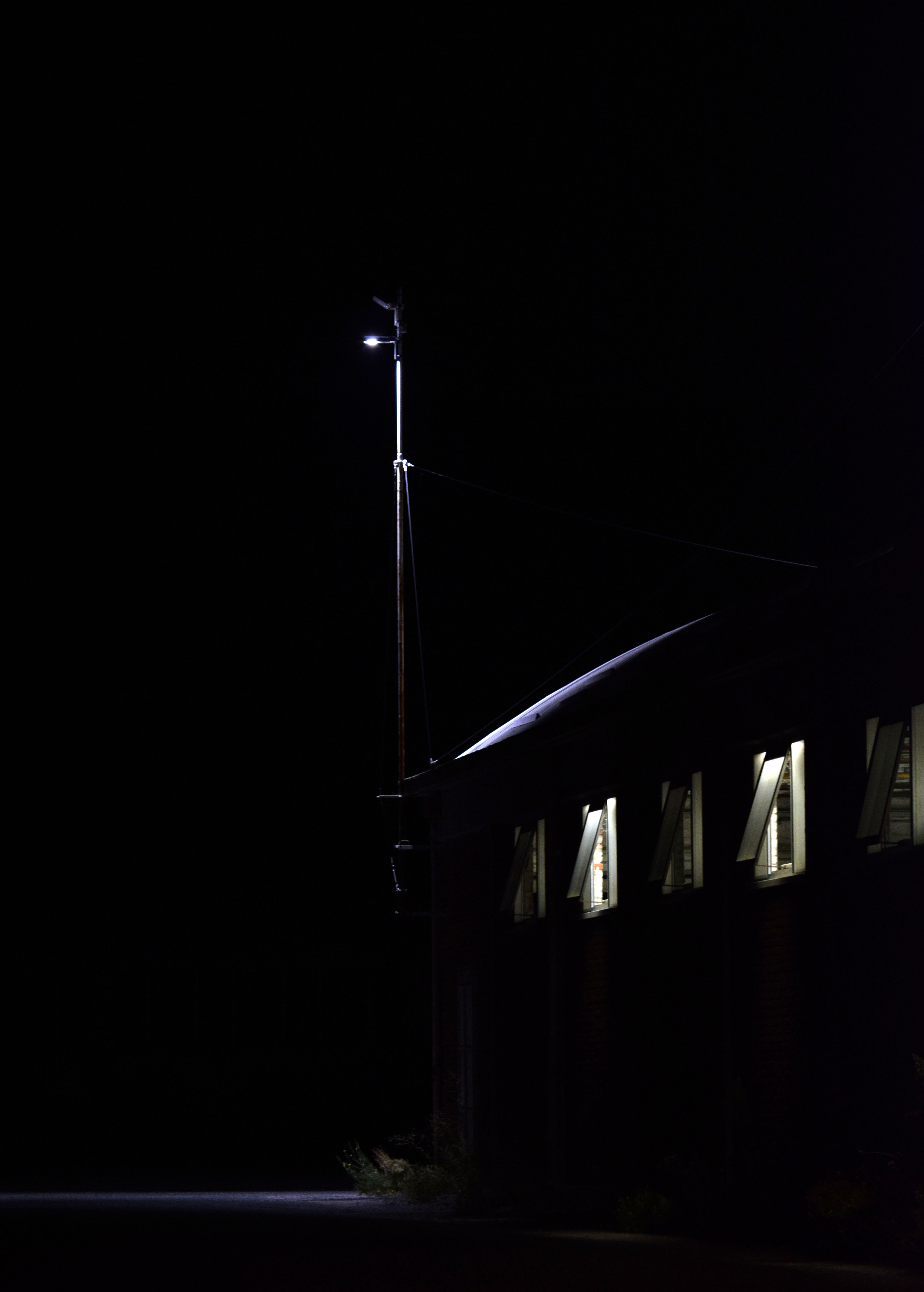 Fotografia di un capannone, finestre illuminate e un palo della luce che illumina poco