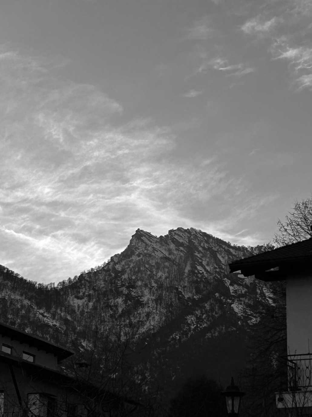 La fotografia è in bianco nero e mostra una montagna con della neve su di essa e un cielo con delle nuvole